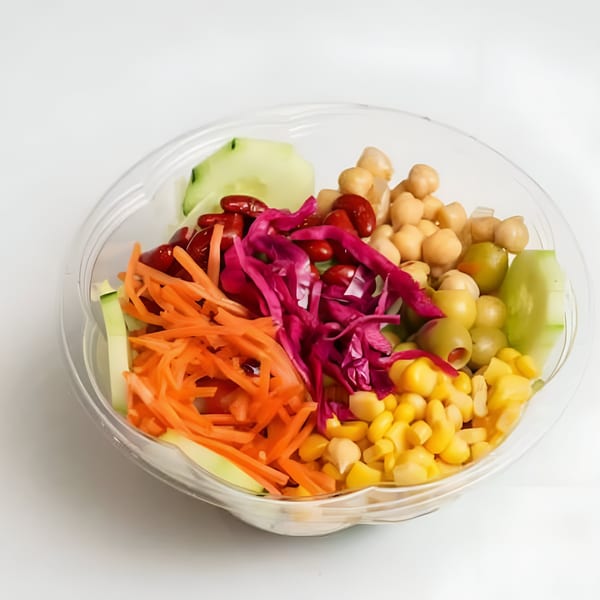 Colorful halal salad in a clear plastic bowl with shredded carrots, red cabbage, chickpeas, corn, and olives.